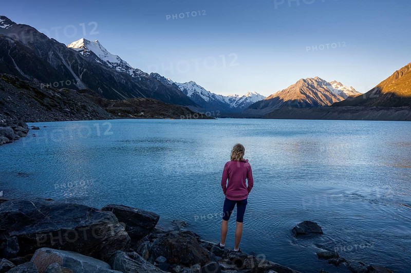 A woman is standing on the shores of Tasman Lake. On the left, Mount Cook. Golden hour. Aoraki Mount Cook National Park, Canterbury, South Island, New Zealand