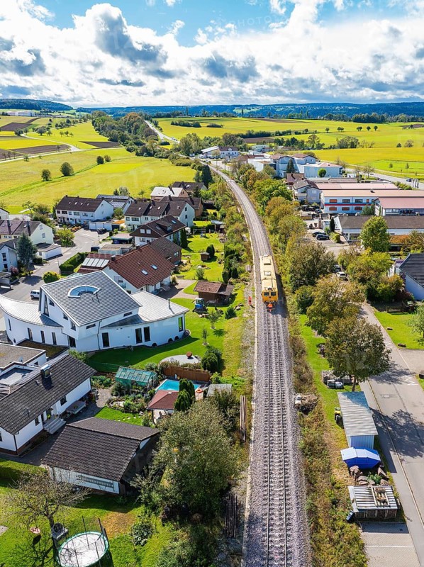 Yellow train travelling through a village surrounded by a rural landscape and houses, tamping machine, Hermann Hessebahn, Althengstett, Black Forest, Germany