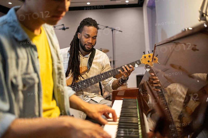 A recording studio scene with musicians collaborating. A pianist focuses on keys while a bassist observes, ready to contribute. Instruments and mics are visible