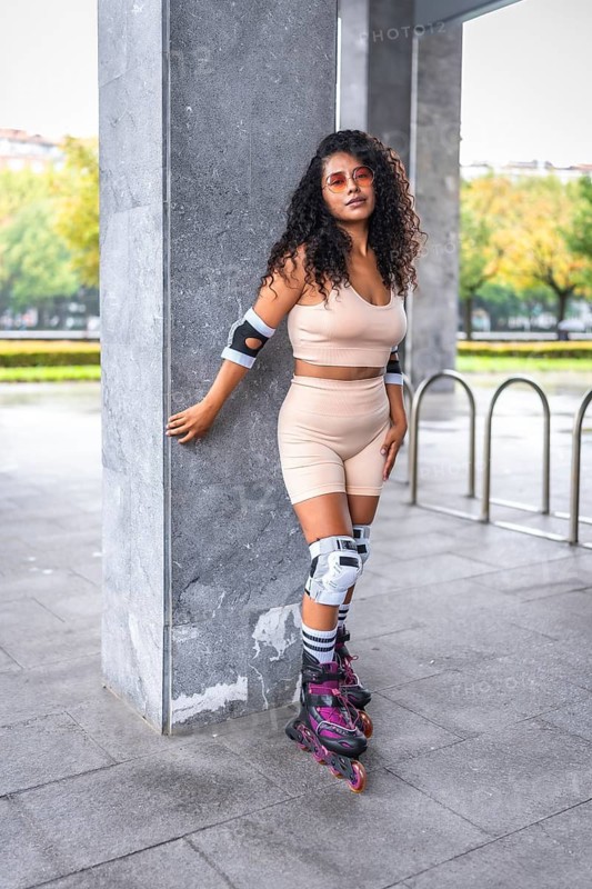 Portrait of a latin female skater with inline skates on a urban park standing leaning on column