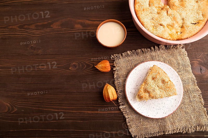 Apple Charlotte cake on brown wooden background and linen textile, cup of milk, top view, flat lay, copy space