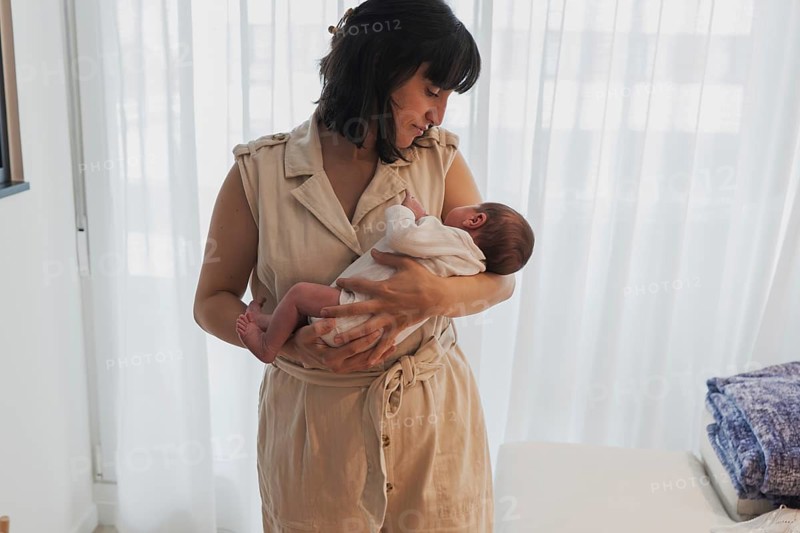 A loving mother cradles her newborn baby in a serene home environment. The intimate moment captures the essence of motherhood and the warmth of family bonds
