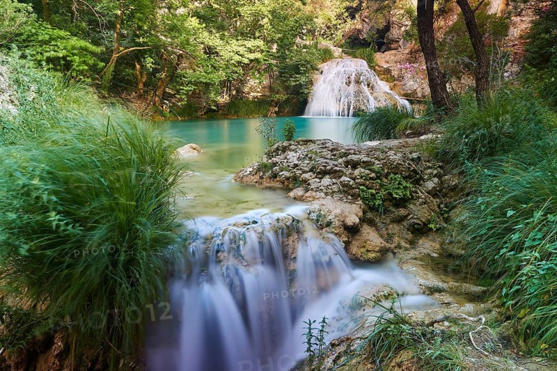 A waterfall flows into a basin surrounded by rocks and green vegetation, in a peaceful setting, waterfalls, ponds, Polylimnio, Peloponnese, Greece