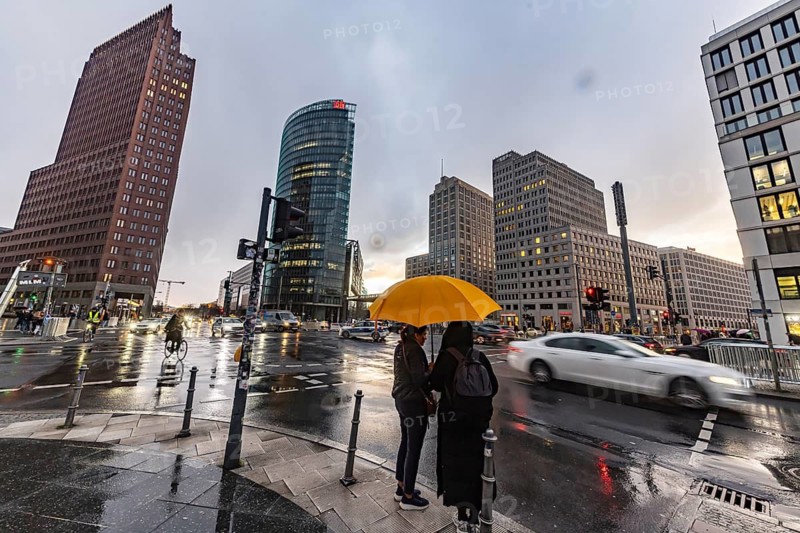 Potsdamer Platz Berlin in the evening with traffic on the streets. When it rains, the skyscrapers are reflected in puddles of water. People traveling with umbrellas. Berlin, Germany