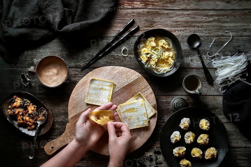 Top view of anonymous woman preparing wonton soup on a wooden table