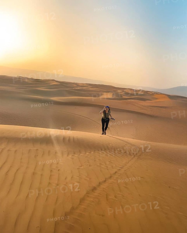 Smiling happy woman running in the vast Wahiba Sands Desert at sunrise, capturing the serene beauty of golden dunes under the clear blue sky in Oman