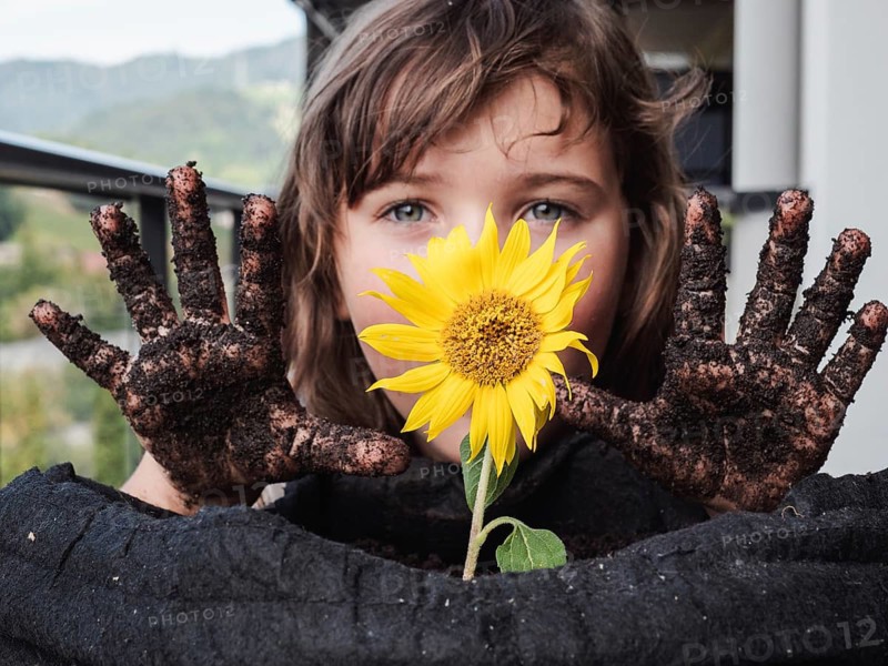A young girl showcases her muddy hands while clutching a bright sunflower, symbolizing the connection between children and nature
