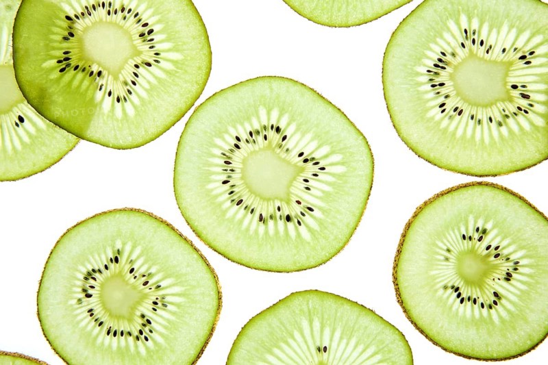 Close up of vibrant kiwi slices arranged on a light background. The image showcases the bright green flesh and small black seeds, highlighting freshness and health