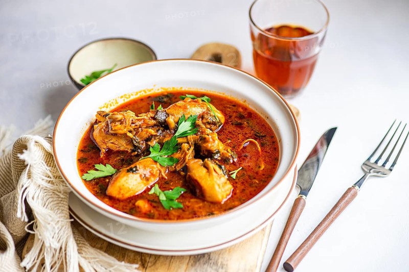 Traditional Georgian chicken stew, known as chakhokhbili, cooked in a rich tomato sauce with paprika and coriander. Served in a bowl, showcasing vibrant colors and fresh herbs