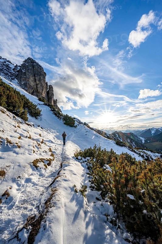 Hikers on a hiking trail with snow, sun star, ascent to Kramerspitz, in autumn, Ammergau Alps, Bavarian Prealps, Bavaria, Germany