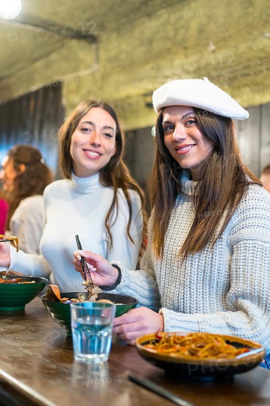 Vertical photo of two stylish women eating ramen soup in a restaurant