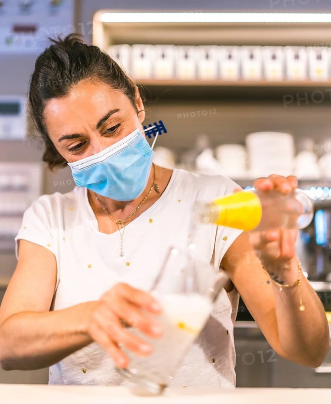 Photo session with a waitress with a face mask in a bar. New normality, security measures after the coronavirus pandemic, social distance, covid-19. Making a soft drink with ice