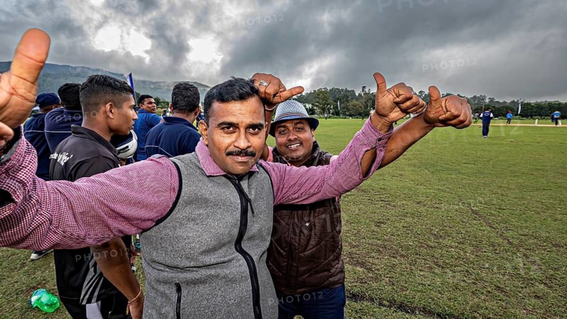 Two men give thumbs up on a sports field with cloudy skies, people and fans playing sports in Nuwara Eliya Sri Lanka