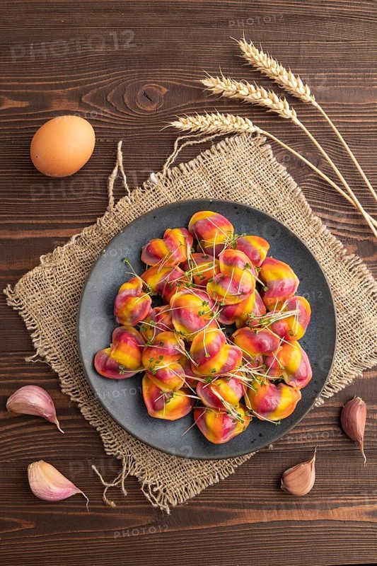 Rainbow colored dumplings with pepper, herbs, microgreen on brown wooden background and linen textile. Top view, flat lay, close up