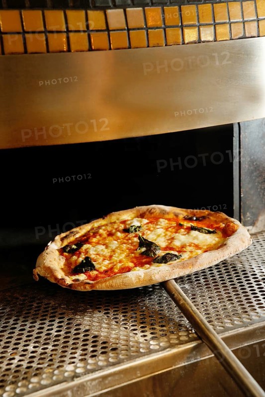 A freshly baked pizza with basil and cheese topping out of an industrial pizza oven