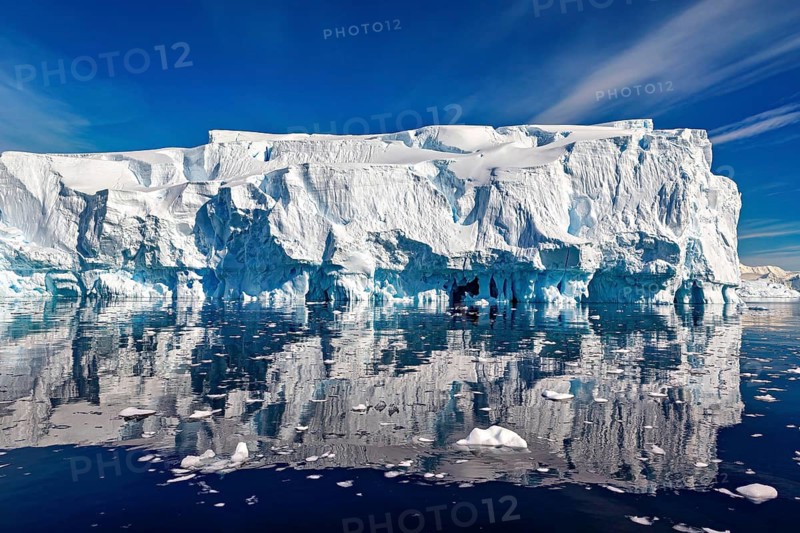 Impressive ice formations are reflected in the calm sea under a clear sky, icebergs in the Southern Ocean in the Antarctic