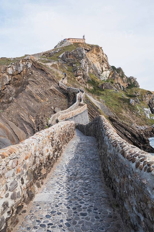 A winding stone pathway leads to a historic hermitage dedicated to Saint John the Baptist atop Gaztelugatxe, a dramatic islet in Bermeo, Basque Country, Spain