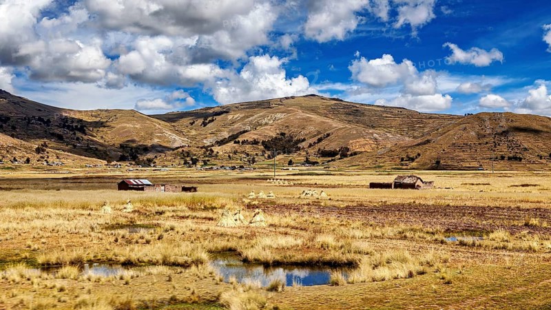 Scattered huts and swampy areas under a mountainous and cloudy landscape, The villages and countryside near Puno in Peru