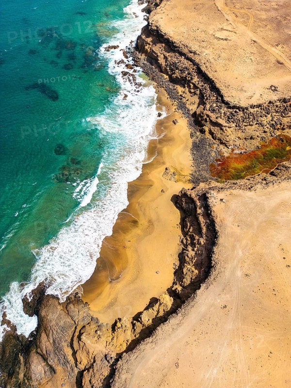 Top view of Tindaya Beach on Fuerteventura Island, featuring untouched sandy shores and rocky cliffs, surrounded by clear turquoise waters and natural pools, captured via drone