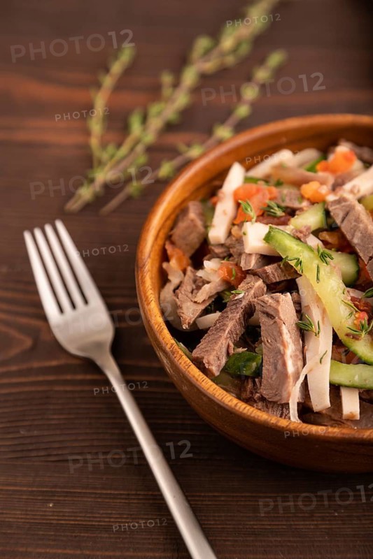 Meat salad with beef and vegetables in wooden bowl on brown wooden background and linen textile. side view, close up, selective focus