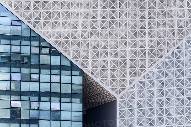 A striking view of modern architecture in Tbilisi, showcasing a detailed geometric facade contrasted with a grid of glass windows, emphasizing urban design innovation