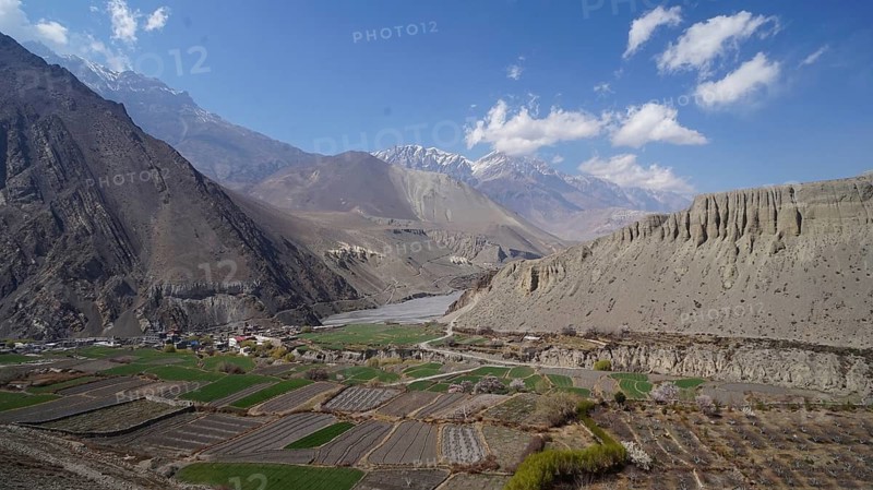 View of a green valley surrounded by high mountains under a slightly cloudy sky, trekking at Annapurna Circuit, Nepal