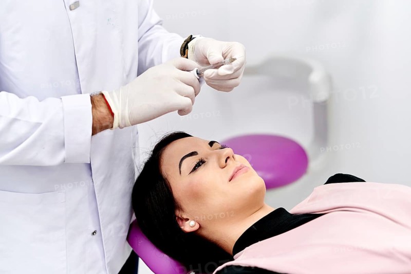 A patient receives a facial cosmetic treatment in a medical clinic. The doctor prepares for the procedure, ensuring a safe and effective application for aesthetic enhancement
