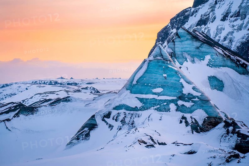Vibrant sunset light washes over jagged blue ice formations at Katla Glacier in Iceland. The vivid contrast of glowing skies and icy textures captures the raw beauty of this arctic landscape