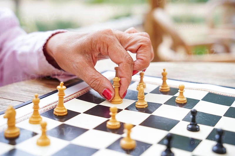 A hand strategically moves a chess piece on a board during an outdoor game The setting emphasizes the focus and strategy involved in this classic game Natural elements surround the scene
