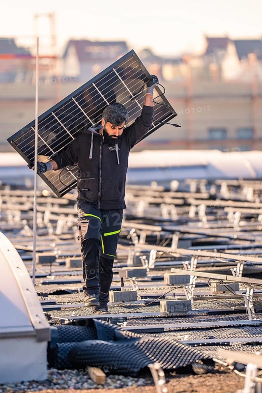 A worker carries a solar panel on a roof in clear weather, PV installation at OBI Baumarkt, Mühlacker, Enzkreis, Germany