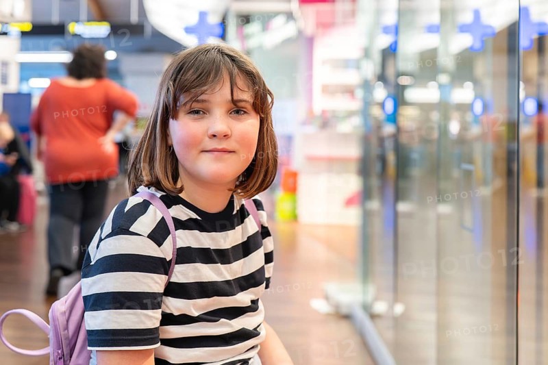A teen girl with a backpack waits in an international airport terminal. The bright, modern environment highlights the excitement and anticipation of travel and exploration