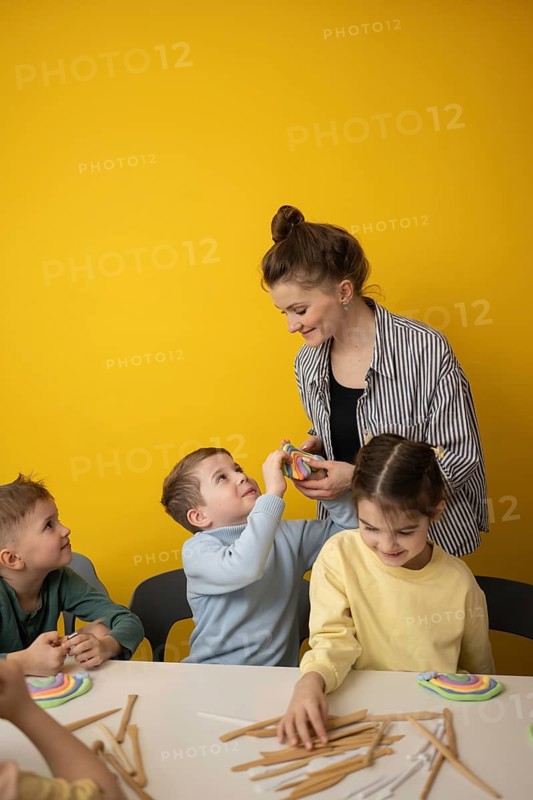 Engaged children participate in a fun, interactive lesson with their teacher. Surrounded by colorful crafts and tools, they explore creativity in a lively environment