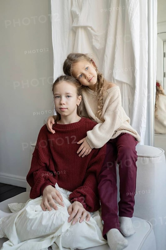 Two young sisters share a tender moment at home, dressed in cozy sweaters The loving embrace captures their bond against a soft, neutral backdrop
