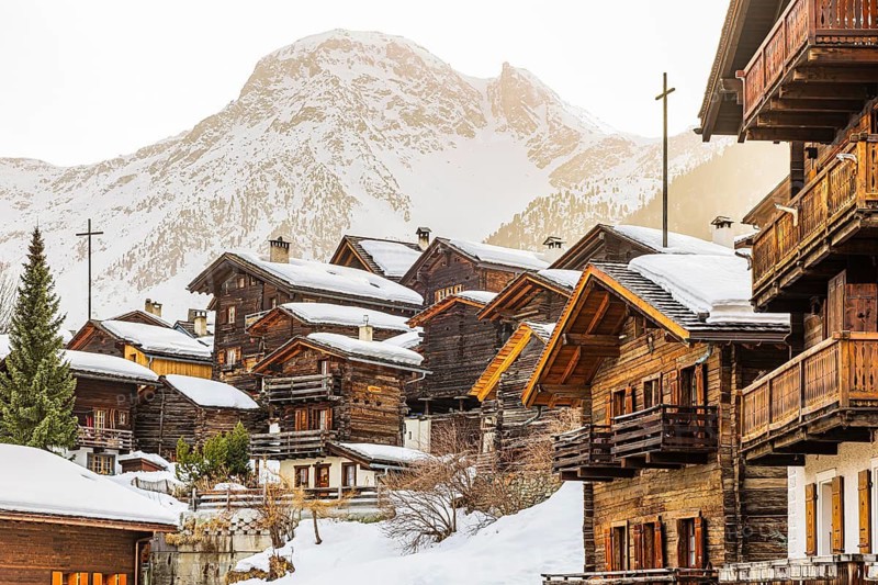 Snow-covered old farmhouses, large wooden cross, historic town center, in the back the snow-capped summit of Sex de Marinda, Grimentz, Val d'Anniviers, Valais Alps, Canton of Valais, Switzerland