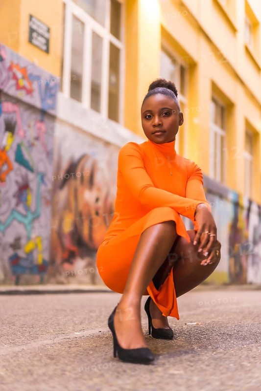 Fashionable urban style with a black African girl in an orange dress and black heels on a city street