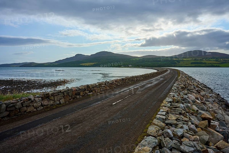 A rocky road stretches through a seascape with twilight sky and mountains in the background, Tongue Lairg, Scotland, United Kingdom, Great Britain