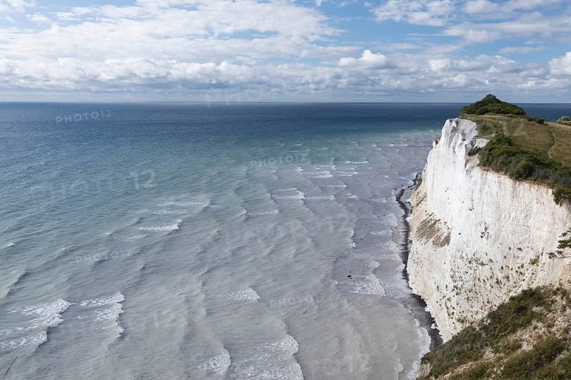 White chalk cliffs at Hundevængsfald with a view of the Baltic Sea towards Møn Lighthouse under a clear blue sky. Møns Klint, Region Sjælland, Denmark