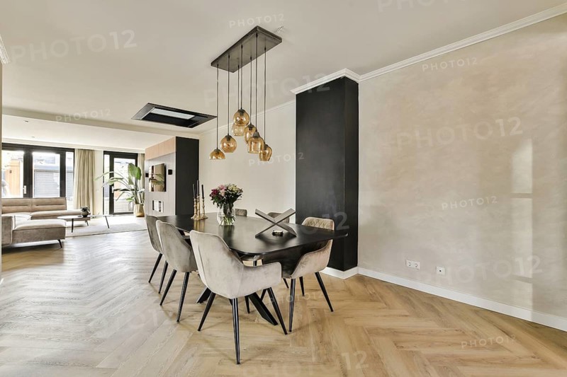 A stylish dining space featuring a wooden table, elegant pendant lighting, and a cozy sofa area. Natural light enhances the ambiance, creating a welcoming atmosphere