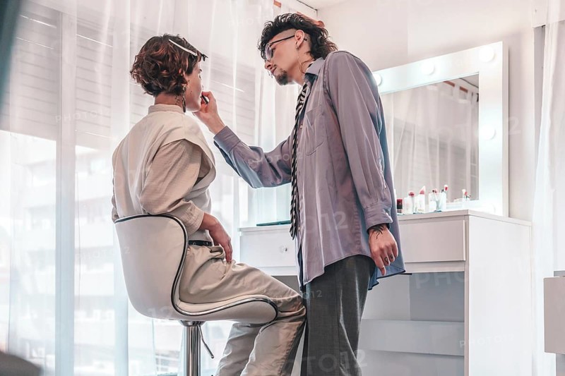 Professional makeup artist carefully applying lipstick on a client sitting in a chair in front of a mirror in a bright and modern beauty salon, showcasing diversity and inclusion