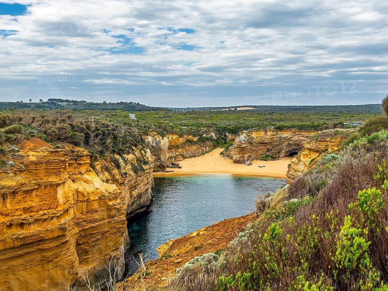 Explore this stunning coastal landscape featuring dramatic cliffs and a serene sandy beach, under a vast, cloudy sky in the Twelve Apostles, Australia. Ideal for nature and travel enthusiasts