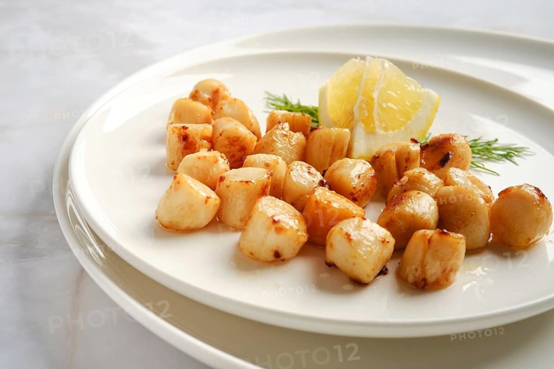 Scallops are cooked and arranged on a white plate. Fresh lemon and herbs add flavor to the dish. This is a seafood meal, suitable for lunch or dinner, ready to be served