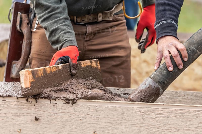 Construction Worker Leveling Wet Cement Into Wood Framing