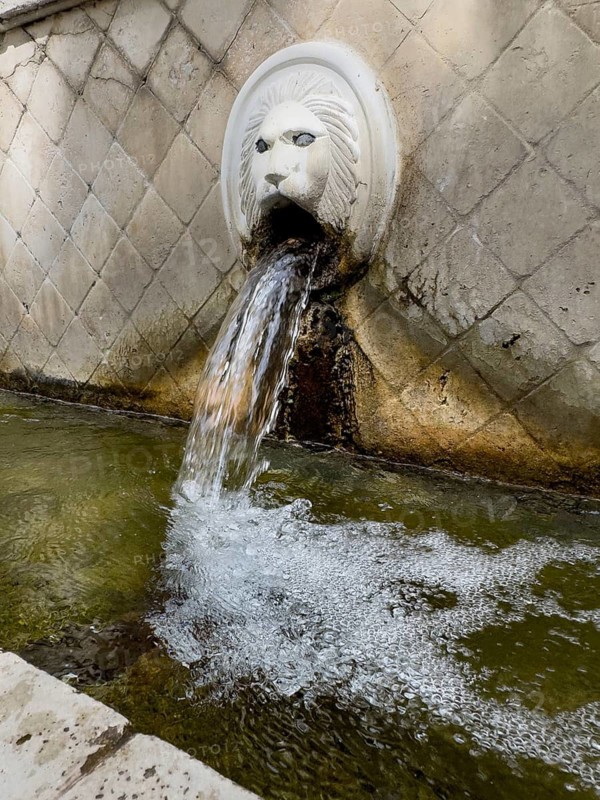 Partial view of large in the picture gargoyle in the form of head of lion lion head below collecting basin of lion fountain Venetian fountain Kefalovrisi with 25 gargoyles for with drinking water on main square of village Spili, Spili, Crete, Greece