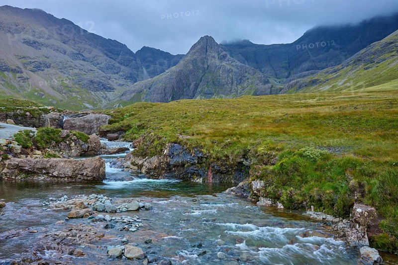 River flows through green valley plain in a mountainous landscape under cloudy sky, Fairy Pools, Grula, Isle of Skye, Scotland, United Kingdom, Great Britain