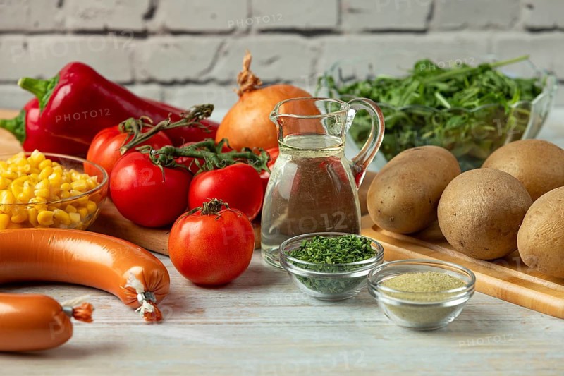Fresh ingredients such as potatoes, tomatoes, peppers, sausage, corn, onions and arugula in a bright environment