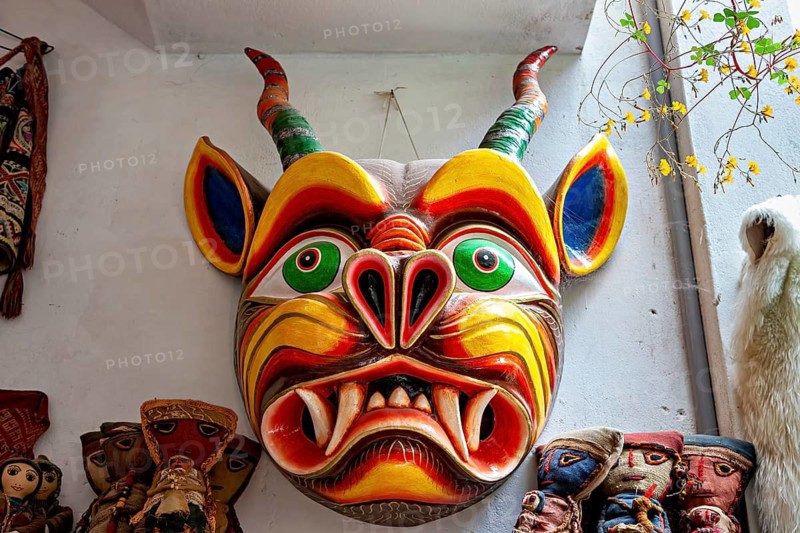 Colourful Tibetan demon mask with bright colors and creepy features on a white wall, masks of mythical creatures in Ollantaytambo in the Andes of Peru