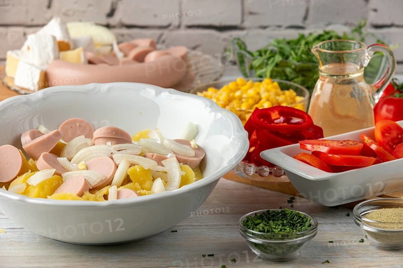 Potatoes, onions and sausage in a bowl surrounded by other ingredients such as peppers, corn, cheese and arugula
