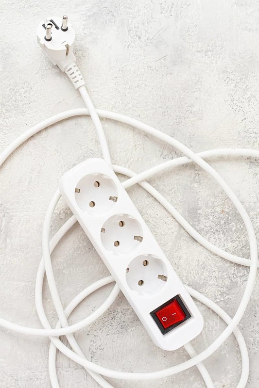 Power strip with multiple sockets and a switch in a cluttered setup on a textured surface during daytime