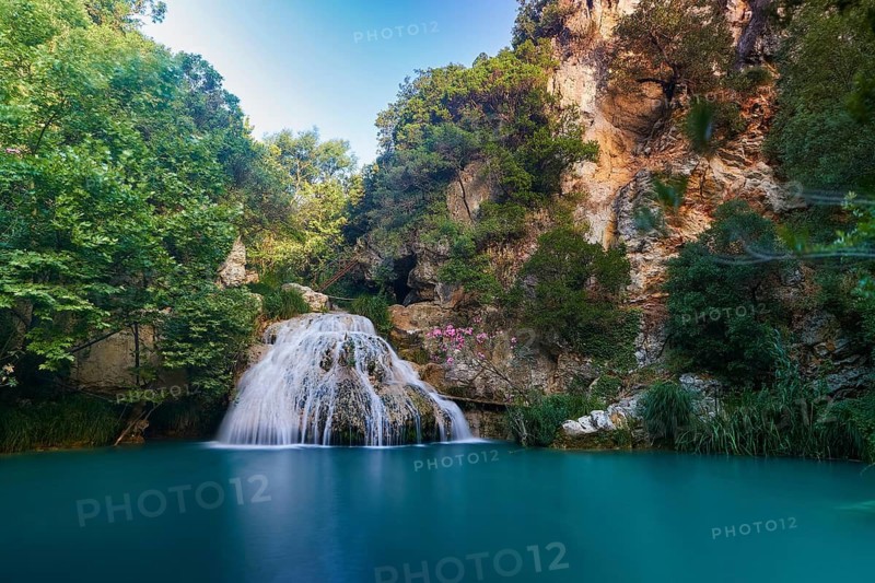 A waterfall falls into a turquoise-blue basin surrounded by green trees and rocky cliffs, waterfalls, ponds, Polylimnio, Peloponnese, Greece