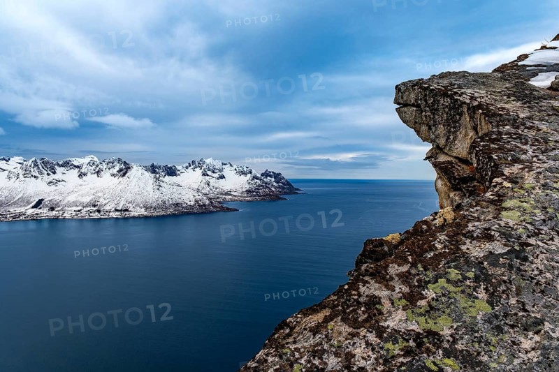 View over rocks to Mefjorden fjord and snowy mountains behind it, Senja island, Troms, Norway